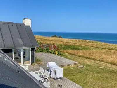 a house with a table and chairs and the ocean at Holiday Home Alkmar - 75m from the sea by Interhome in Thisted