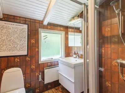 a bathroom with a sink and a toilet and a window at Holiday Home Weland - 800m from the sea by Interhome in Løkken