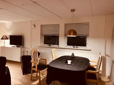 a dining room with a table and chairs and two windows at Gittes hus in Skive