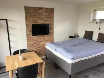 a bedroom with a bed and a table and a tv at Casa Uno North - Nice appartement for two with sea view in Farsø