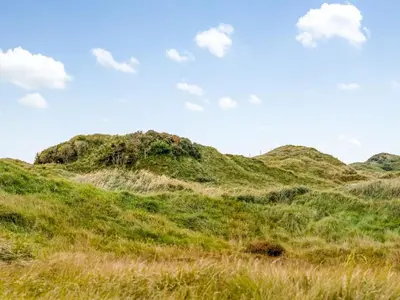 a grassy hill with a blue sky and clouds at Holiday Home Tarvo - 400m from the sea by Interhome in Pandrup