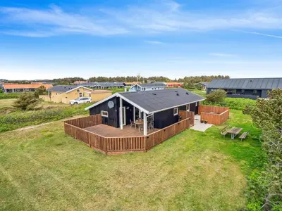 a black house with a deck on a field at Holiday Home Wolter - 700m from the sea by Interhome in Harboør