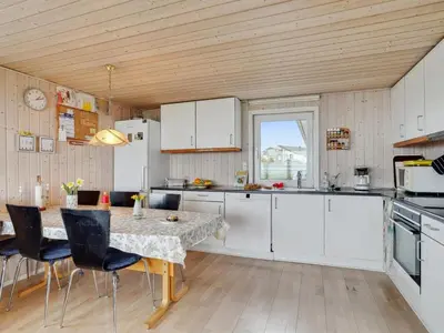 a kitchen with white cabinets and a table with chairs at Holiday Home Ormar - 100m to the fjord by Interhome in Lemvig