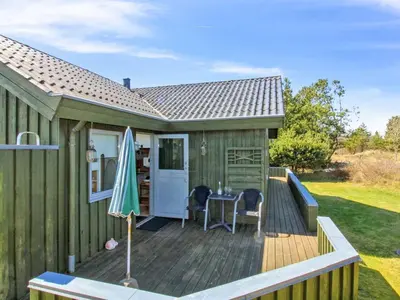 a wooden deck with a table and an umbrella at Holiday Home Gerasim - 1km from the sea by Interhome in Saltum