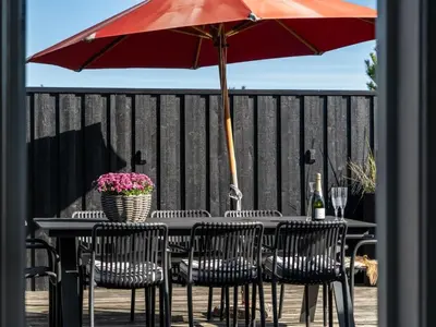 a table and chairs with a red umbrella on a deck at Holiday Home Sazdo - 1-1km from the sea by Interhome in Saltum