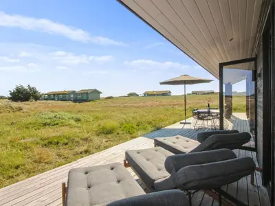 a deck with chairs and a table and an umbrella at Holiday Home Ascan - 600m from the sea by Interhome in Løkken