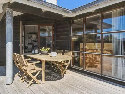 a wooden table and chairs on the deck of a house at Holiday Home Fridgerd - 250m from the sea by Interhome in Blokhus