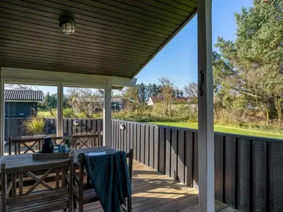 a wooden deck with a table and a dining table at Holiday Home Apsolon - 600m from the sea by Interhome in Løkken