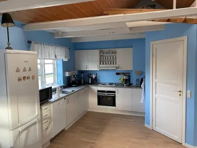 a kitchen with white cabinets and a blue wall at Agger Beach Apartment in Vestervig