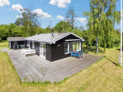 a black cabin with a deck in a field at 6 person holiday home in Nykøbing M-By Traum in Alsted