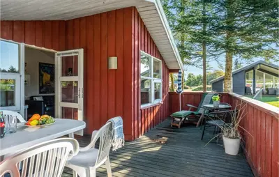 a red house with a wooden deck with a table and chairs at Holiday Home Blokhus 9 in Blokhus