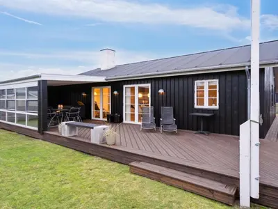 a black house with a large wooden deck at Holiday Home Svante - 600m from the sea by Interhome in Blokhus