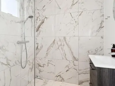 a bathroom with a shower with white marble walls at Holiday Home Scalli - 1-5km to the fjord by Interhome in Farsø