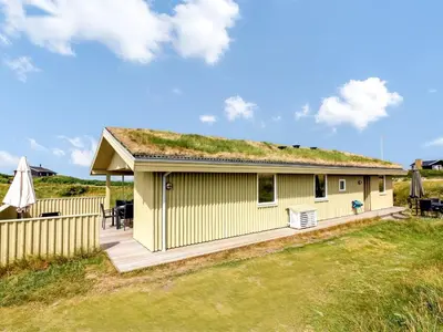 a yellow house with a grass roof with a deck at Holiday Home Pinja - 400m from the sea by Interhome in Løkken