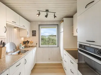 a kitchen with white cabinets and a window at Holiday Home Pinja - 400m from the sea by Interhome in Løkken