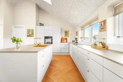 a kitchen with white cabinets and a wooden floor at Uniquely located wooden cottage by the sea - SJ1 in Harboør