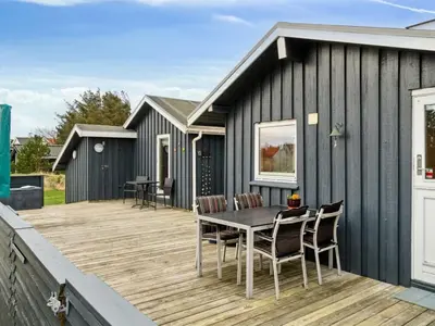 a black house with a wooden deck with a table and chairs at Holiday Home Dolores - 200m from the sea by Interhome in Torsted