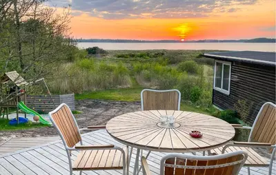 a wooden table and chairs on a deck with the sunset at 2 Bedroom Awesome Home In Højslev in Højslev