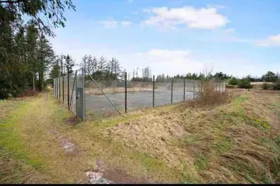 a fence in a field with a tennis court at Pool summerhouse in Saltum near Blokhus in Saltum
