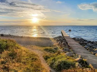 a wooden pathway leading to the ocean with the sun setting at 6 person holiday home in Farsø-By Traum in Farsø
