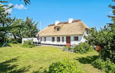 a house with a thatched roof with a yard at 4 Bedroom Nice Home In Blokhus in Blokhus