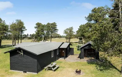 a black building in a field with trees at Røgegård Hjortehytten in Fjerritslev