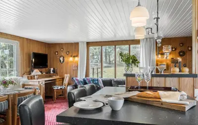 a dining room with a table and chairs and a kitchen at Røgegård Hjortehytten in Fjerritslev