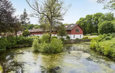 a river in front of a red barn and a house at Hus 1 in Brovst