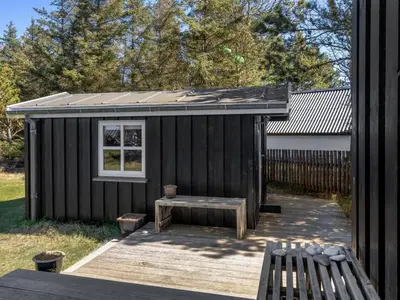 a small black shed with a bench on a deck at Holiday Home Hellena - 700m from the sea by Interhome in Torsted