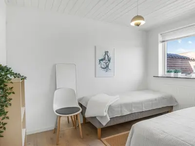 a white bedroom with a bed and a chair at Holiday Home Sulo - 300m from the sea by Interhome in Blokhus