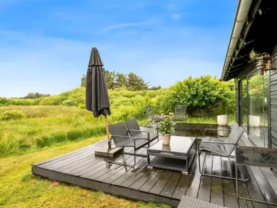 a deck with an umbrella and chairs and a table at Holiday Home Mintha - 400m from the sea by Interhome in Blokhus