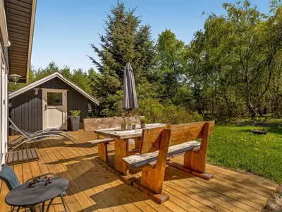a wooden deck with a table and an umbrella at Holiday Home Hermand - 3-5km from the sea by Interhome in Brovst
