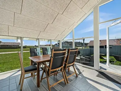 a wooden table and two chairs on a patio with windows at Holiday Home Emppu - 250m from the sea by Interhome in Harboør