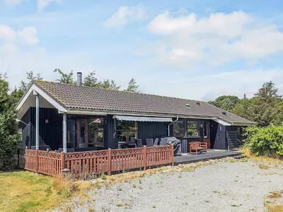 a black house with a wooden deck on a field at 4 star holiday home in Øster Assels-By Traum in Øster Assels