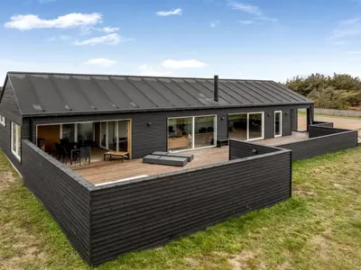 a black house with a deck in a field at Holiday Home Dreng - 300m from the sea by Interhome in Harboør