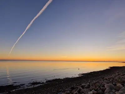 a jet contrail flying over the water at sunset at 4 person holiday home in Hurup Thy-By Traum in Sindrup