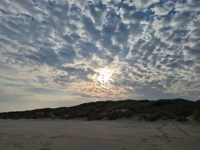 a cloudy sky over a beach with the sun in the distance at 6 person holiday home in Blokhus in Blokhus