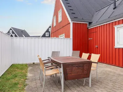 a table and chairs on a patio with a red building at 6 person holiday home in Blokhus-By Traum in Blokhus