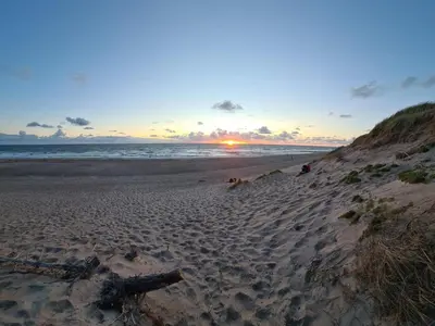 a sunset on a beach with a log on the sand at 8 person holiday home in Ulfborg-By Traum in Thorsminde
