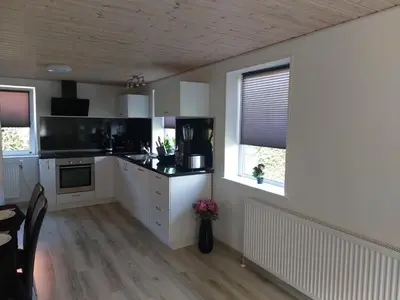 a kitchen with white cabinets and a table and two windows at Venos Home in Lemvig