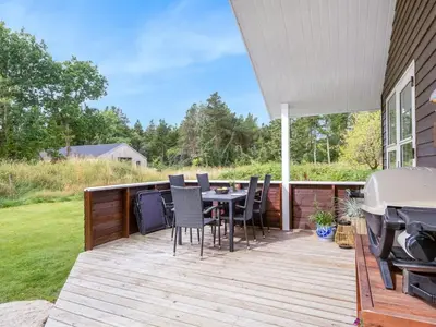 a deck with a table and chairs and a grill at Holiday Home Unge - 2-9km from the sea by Interhome in Blokhus