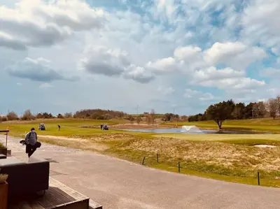 a person sitting on a bench looking at a golf course at Skønt Sommerhus Golfhytte midt i skønne omgivelser in Gatten