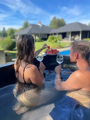 a man and woman sitting in a swimming pool with wine glasses at Aneks i rolige omgivelser-adgang til pool og sauna in Avlum