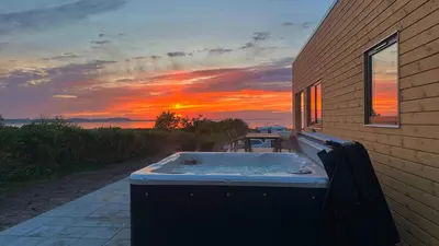 a hot tub sitting outside of a house with a sunset at Premium hytte med udendørs spa in Farsø