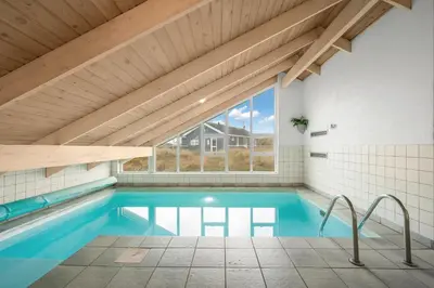 a swimming pool in a house with a wooden ceiling at Pool House With Spa And Sauna, 200 Meters From The North Sea in Frøstrup