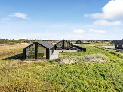 a black house in a field with glass at Holiday Home Stenkil - 1-2km from the sea by Interhome in Løkken