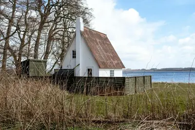 a white house with a brown roof on a grass field at Small House With View Of The Limfjord in Roslev