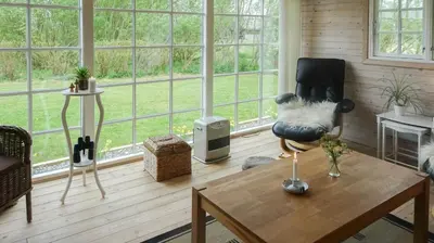 a living room with a chair and a table at Charming Wooden Cottage Close To Handbjerg Beach in Vinderup