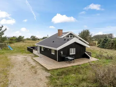 a black house with a deck in a field at Holiday Home Caya - 750m from the sea by Interhome in Løkken
