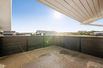 an empty patio with a wooden fence and the sun in the sky at Lovely Holiday Home With Pool, Spa And Sauna, Only 200 Meters From The North Sea in Harboør